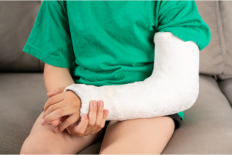 Child with a white forearm cast resting on their lap while sitting on a gray couch, wearing a green shirt